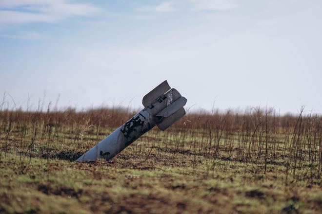 An unexploded rocket is lodged in the ground in the middle of an empty field.