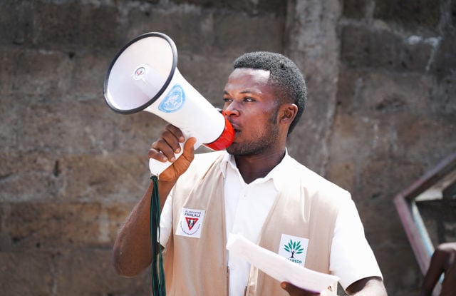 En voksen mann holder en megafon med FN-logo foran en murvegg.