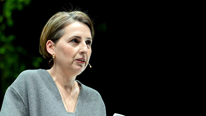  denne En kvinne står innendørs og holder noen ark, med grønne planter i bakgrunnen.