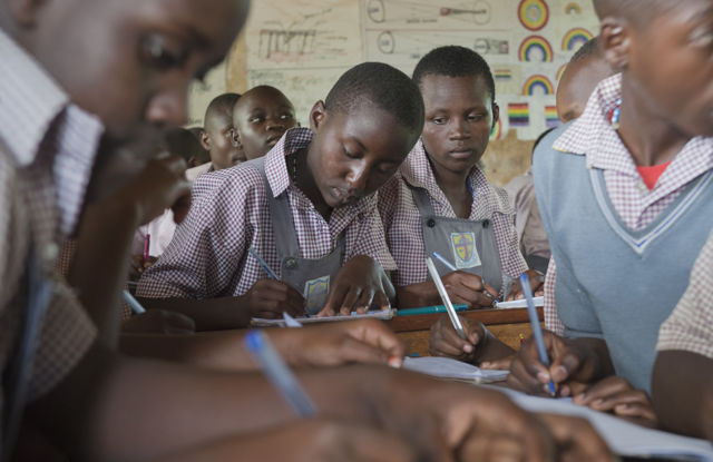 Elevar i skuleuniform skriv ved pultar i klasserom