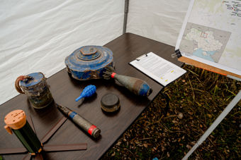 Various types of explosives and unexploded ordnance are displayed on a table next to a map and documents.