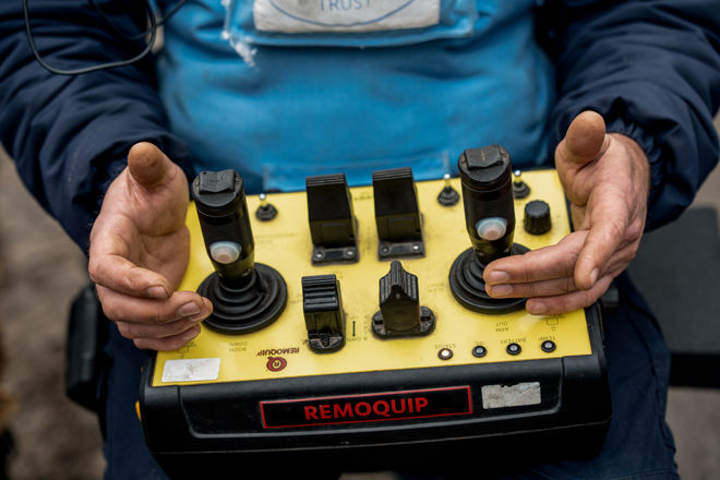 A person in a blue jacket operates a yellow remote control device labeled "REMOQUIP" with both hands.
